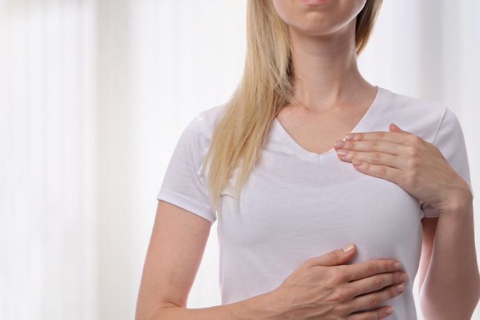 Mujer palpándose el seno izquierdo sobre la ropa