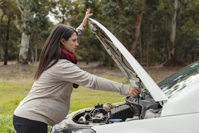 Mujer con varias semanas de embazarlo mirando el motor de su auto.