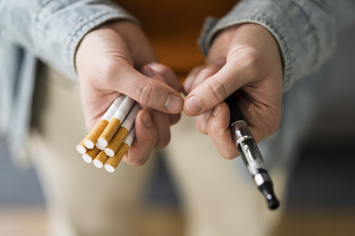 Persona sosteniendo cigarrillos y cigarrillo electrónico