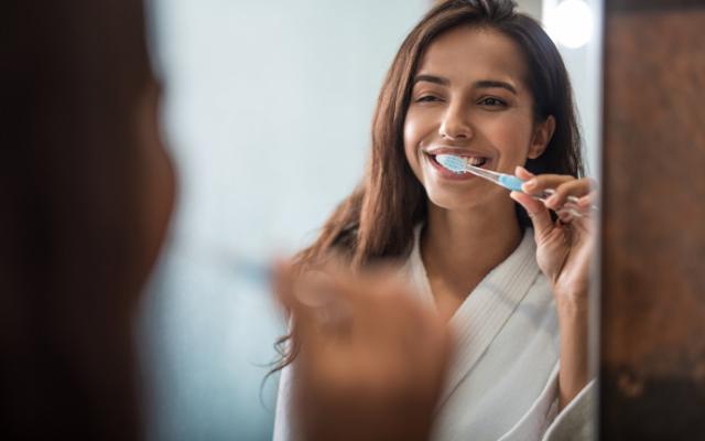 Mujer sonriente lavándose los cfientes delante del espejo