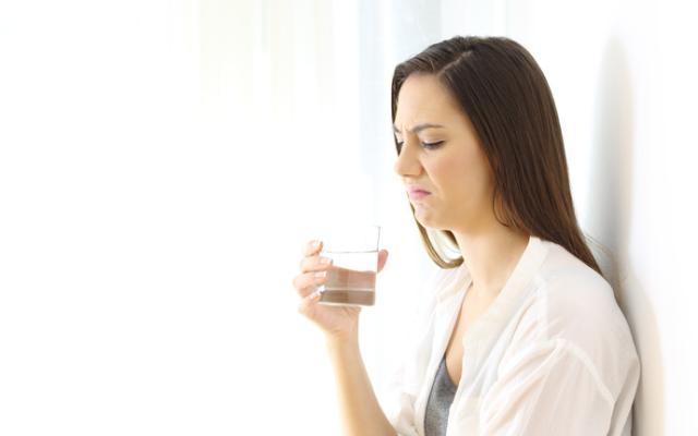 Mujer con sabor metalico en la boca sujetando un vaso de agua