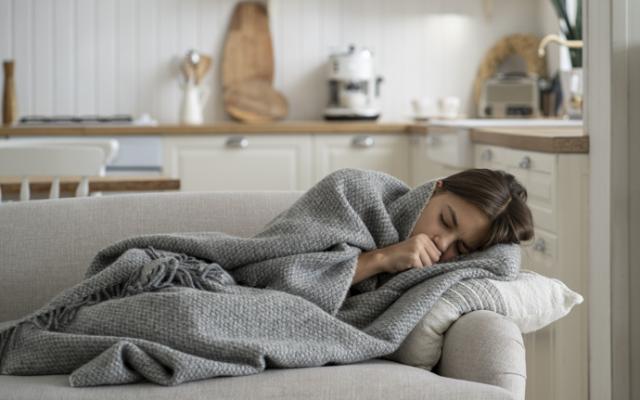 Mujer tumbada en el sofá tapada con manta que sufre escalofríos sin fiebre.