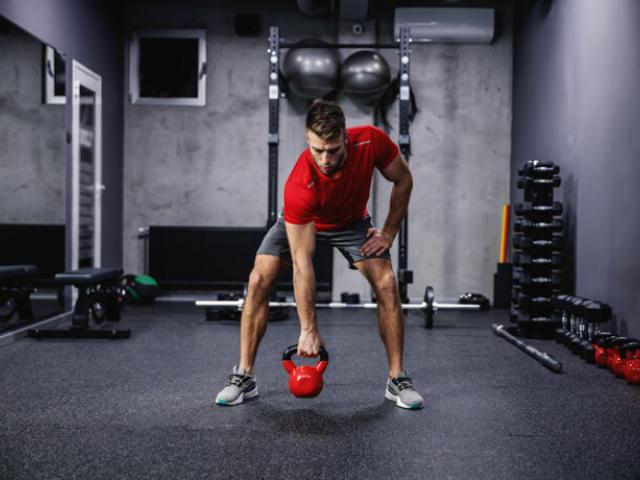 hombre levantando pesa kettlebell en gimnasio