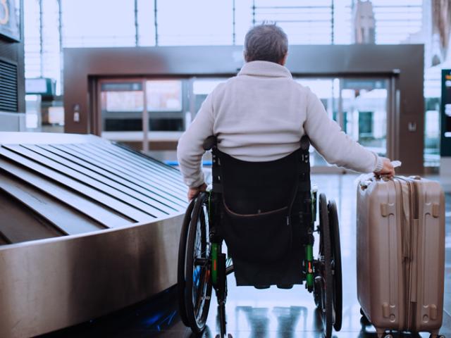 Hombre mayor en silla de ruedas, recogiendo su equipaje en el aeropuerto