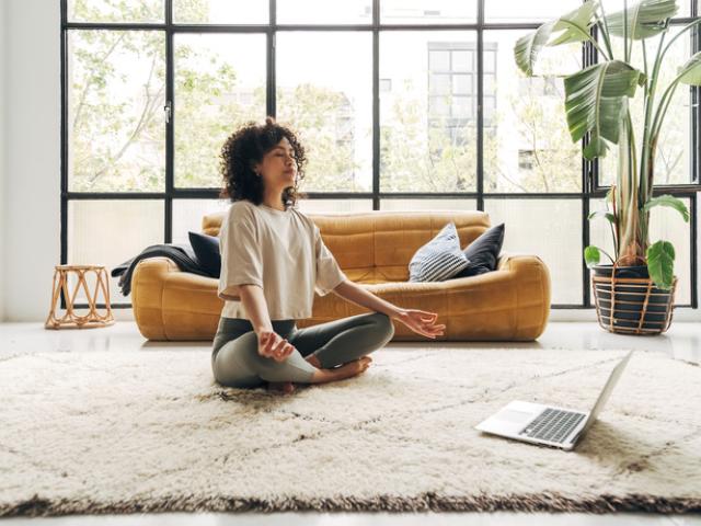 Mujer haciendo una meditación guiada con su computadora sobre una alfombra