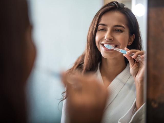 Mujer sonriente lavándose los cfientes delante del espejo