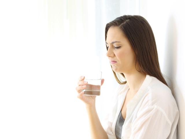 Mujer con sabor metalico en la boca sujetando un vaso de agua