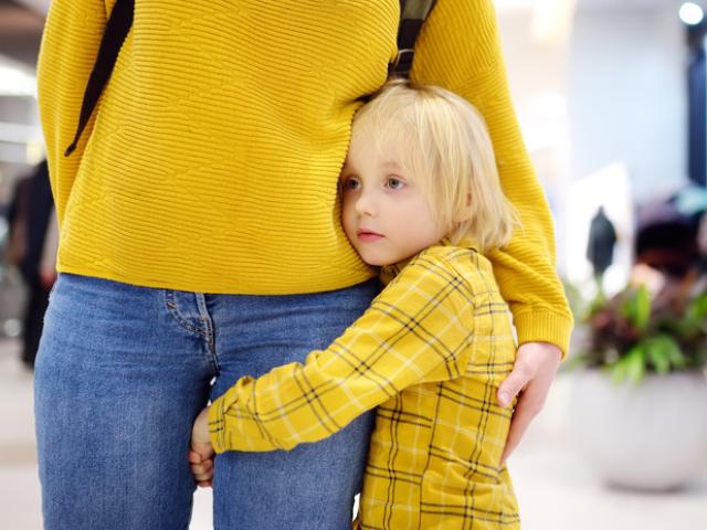 Niña pequeña agarrada a la pierna de su madre